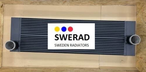 En gråfärgad metallkylare, märkt som "Oljekylare Bruks flishugg", med två identiska runda öppningar på vardera sidan, placerade på en beigefärgad yta.